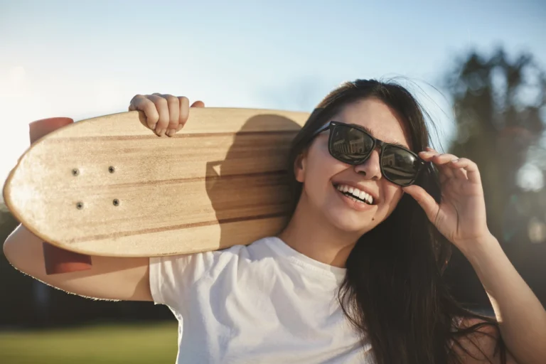 girl wearing sunglasses smiling and holding a skateboard